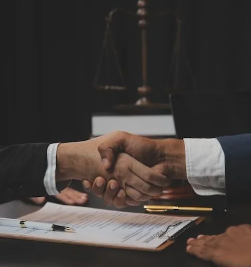 A handshake over legal documents, with the scales of justice in the background